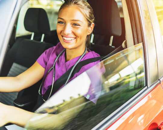 Female nurse in purple scrubs driving a vehicle