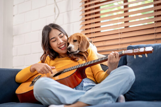 Young woman playing her guitar with her dog